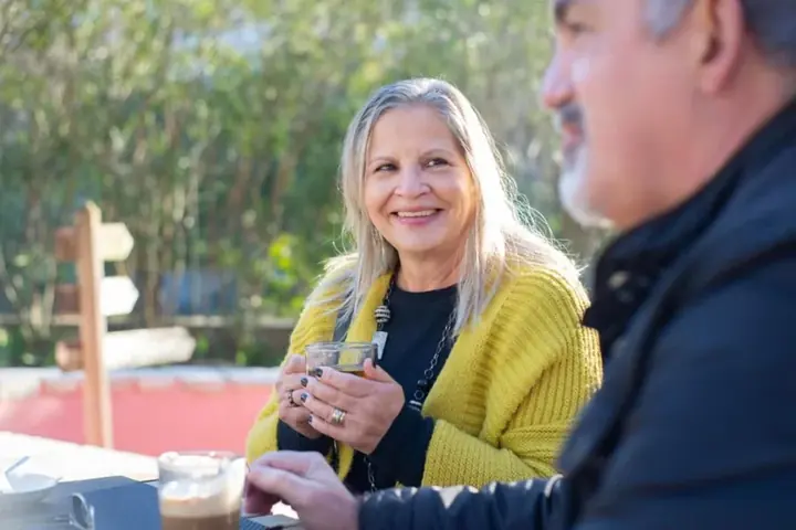 Senhora sorrindo enquanto conversa com um amigo num café