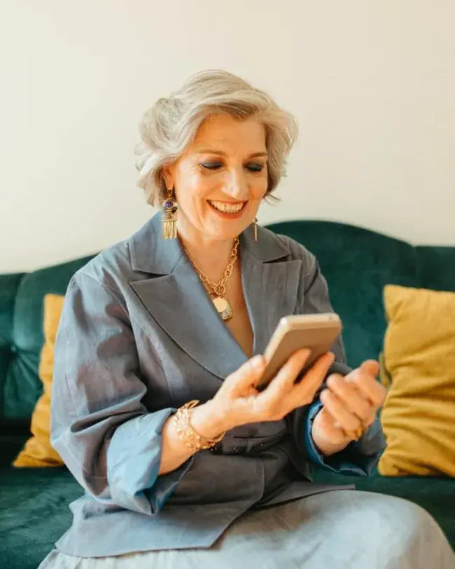 Senhora sorrindo enquanto usa o celular no sofá
