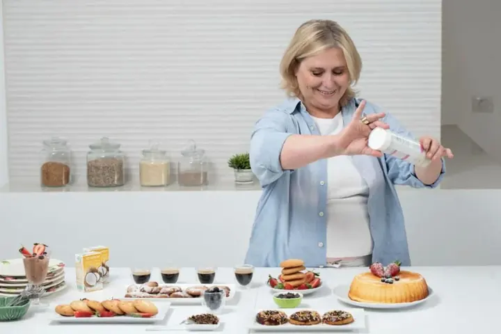 Senhora finalizando doces e um bolo na cozinha